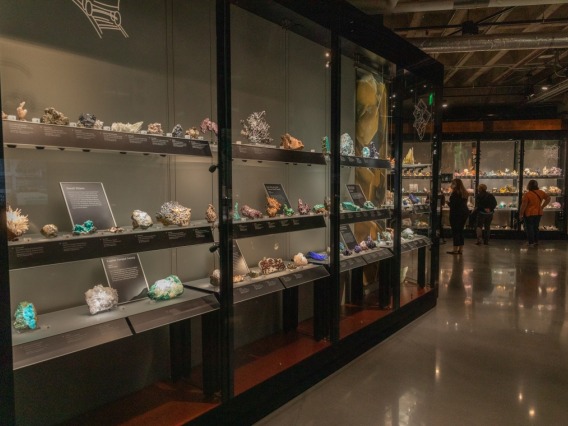 A glass case displaying gem and minerals with three individuals observing exhibits 