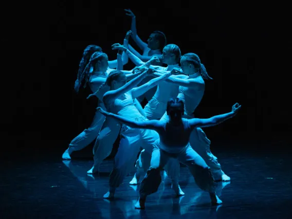 A photograph of dancers forming a facing line under a blue light