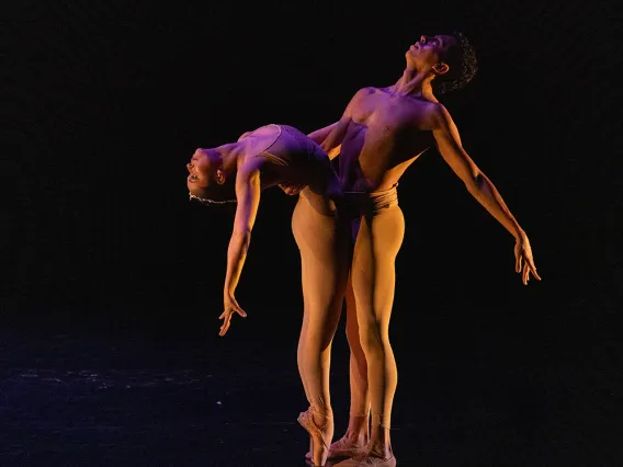 A photograph of two dancers with their bodies pressed against each other and their heads looking up