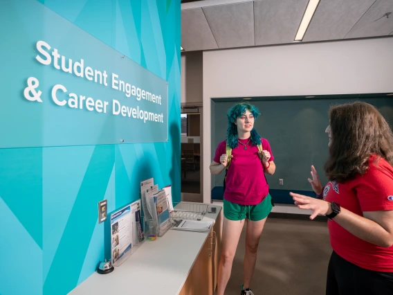 A photo of a student standing in front of the SECD sign while talking to a worker