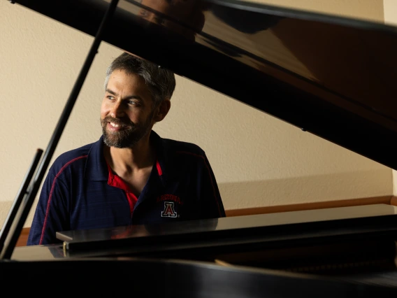 Image of Matthew Mugmon sitting and presumably playing the piano. He is looking to the side and smiling.