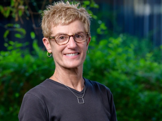 A photo of a woman with short hair, a black t-shirt and brown glasses smiling