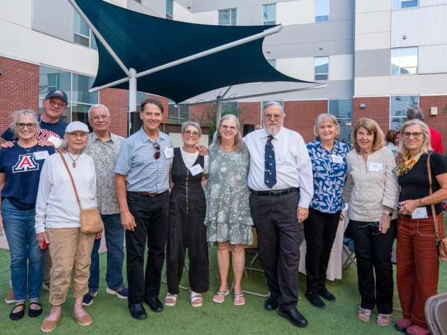 A group of 11 people standing and smiling with their arms around each other at the W.A. Franke Honors College courtyard