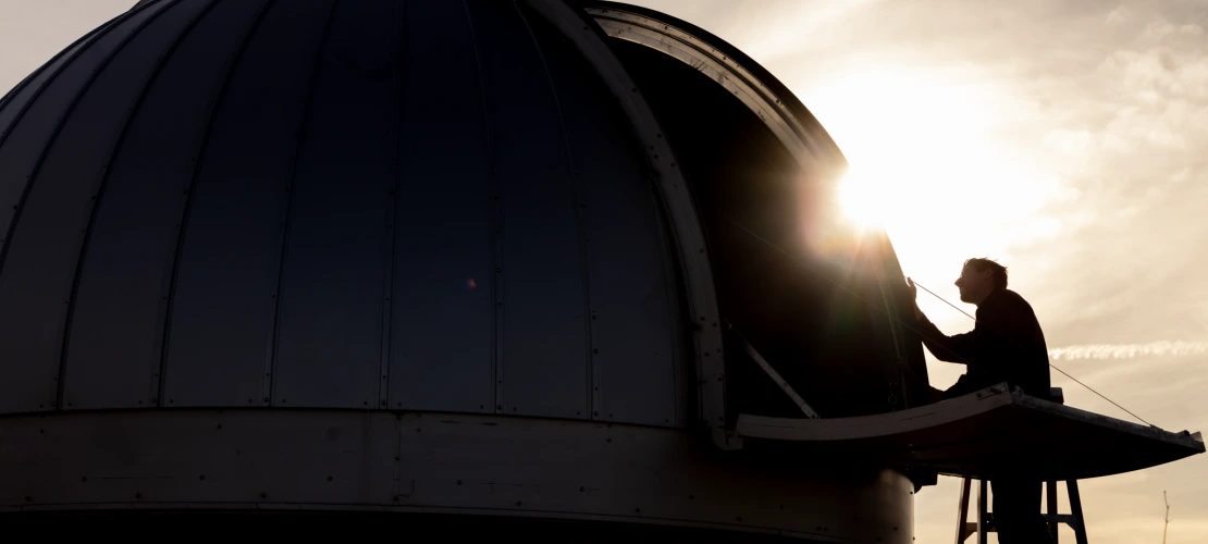 A man standing on a ladder, working on a sensor with the sun beaming behind him 