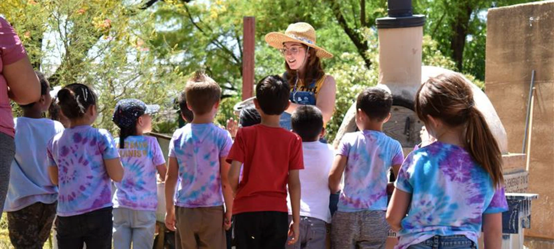 An instructor wearing a sun hat while speaking to children outside
