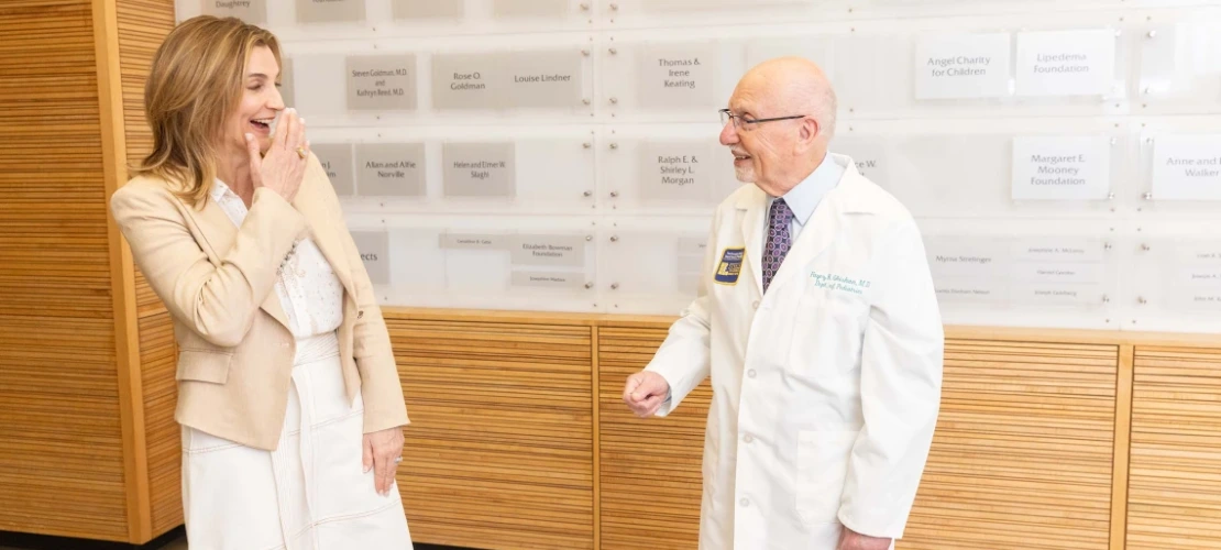 A woman wearing a white dress, smiling and talking to a man wearing a white coat. 