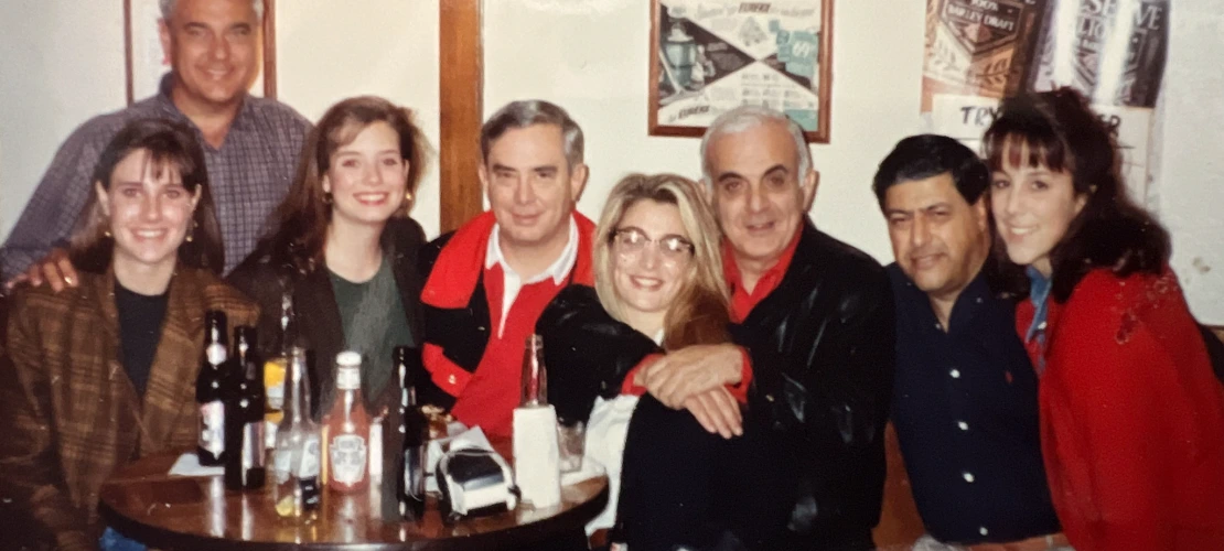 Eight people smiling and hugging at a bar.