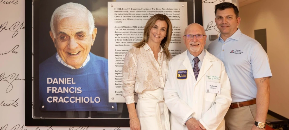 Three people smiling in front of a framed photo of Daniel Francis Cracchiolo 