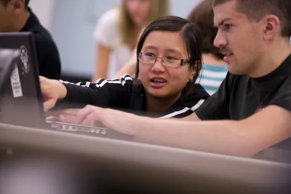 student pointing to a laptop screen as other student looks