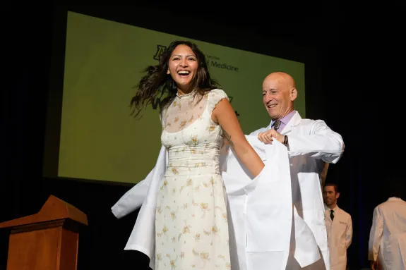 A photograph of a student putting on a white coat and smiling