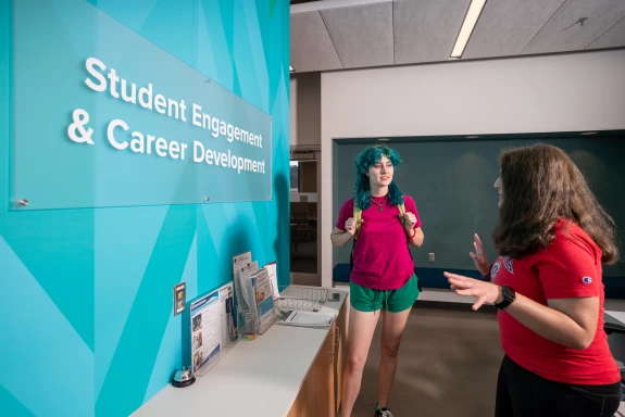 A photo of a student standing in front of the SECD sign while talking to a worker