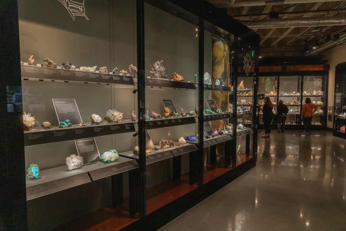 A glass case displaying gem and minerals with three individuals observing exhibits 