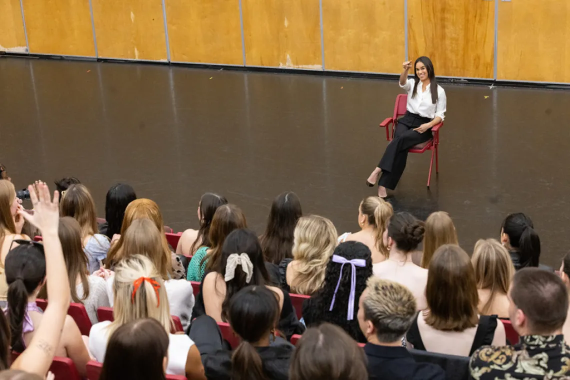 A photo of a woman sitting in a red chair answering students' questions while they sit in a lecture room 