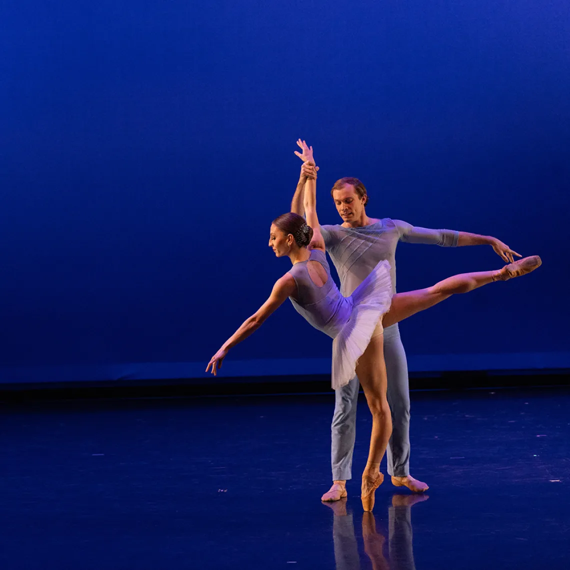 A photograph of one dancer on her tiptoes, being held up by another dancer stretching his body 