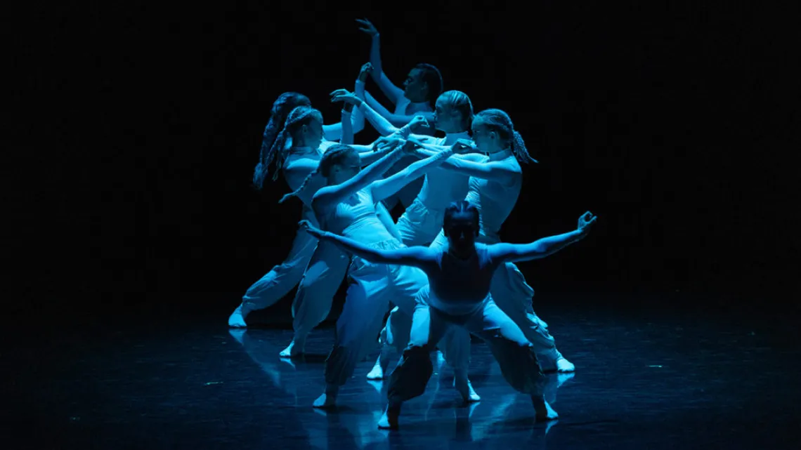 A photograph of dancers forming a facing line under a blue light