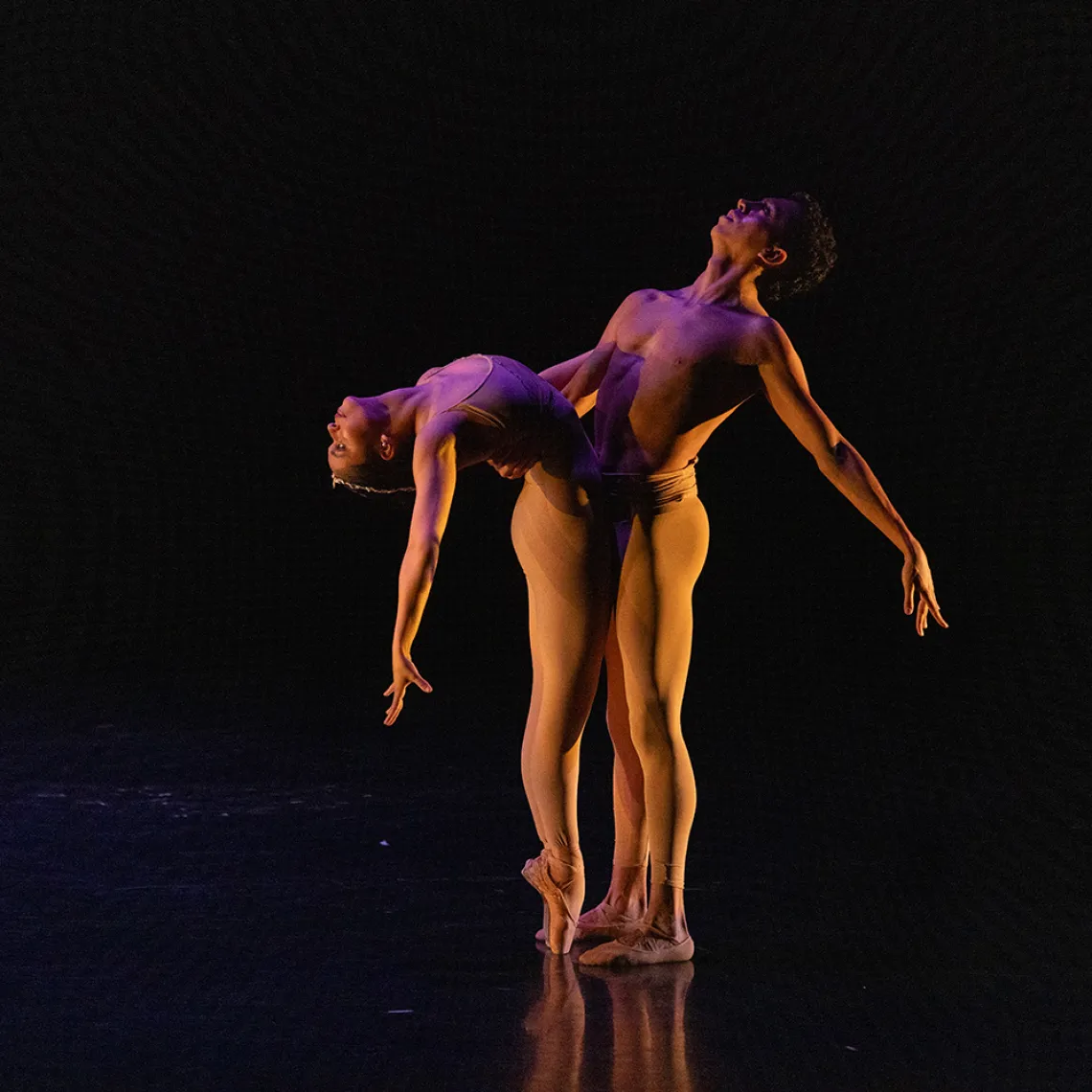 A photograph of two dancers with their bodies pressed against each other and their heads looking up