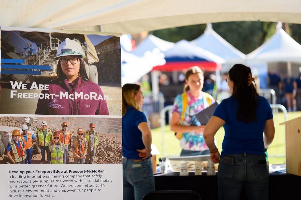 A Freeport-McMoran informational poster with representatives speaking with a student