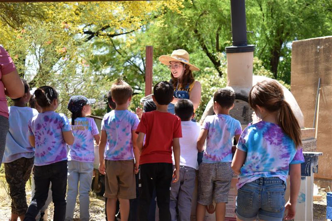 An instructor wearing a sun hat while speaking to children outside