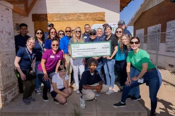 A photograph of 20 people standing and smiling around a giant white and green check 