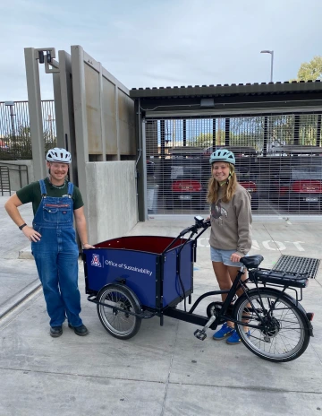 Two students standing and smiling next to an electric bike that says "Office of Sustainability" with a block A